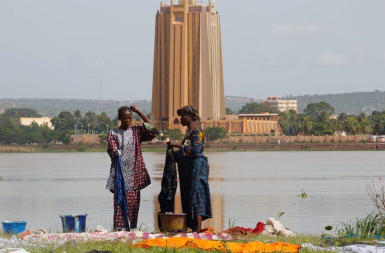 women sort out clothing after doing their washing in the niger river, with the headquarters of central bank of west african states in the background, in bamako